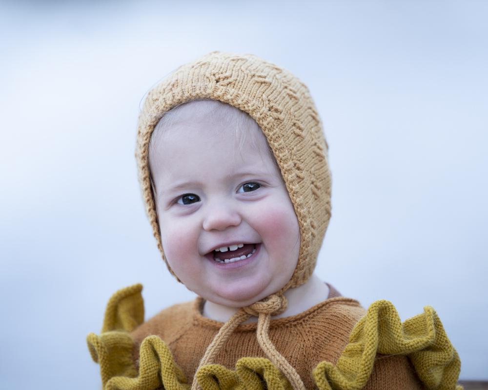 Portrett av en 1 åring. Utefotografering. Jente i oransje og gul kjole og gul kyse. Lilja smiler. Fotograf Maria i Bergen.